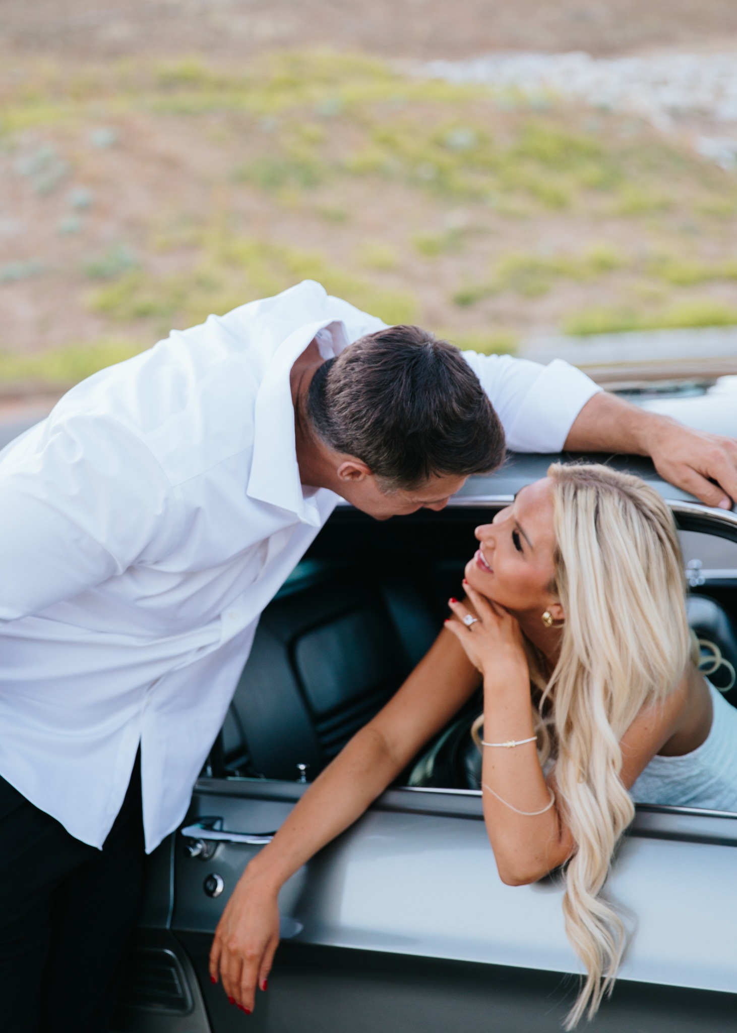 Devin leaning in to kiss Summer beside their classic car