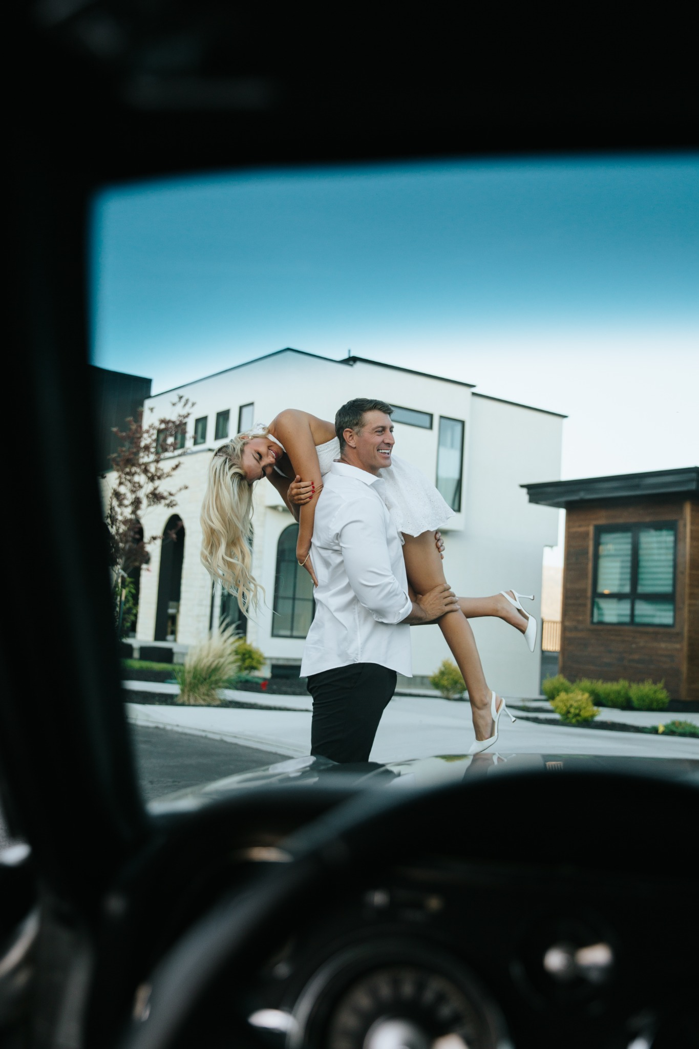 Devin carrying Summer, photographed through their classic Mustang